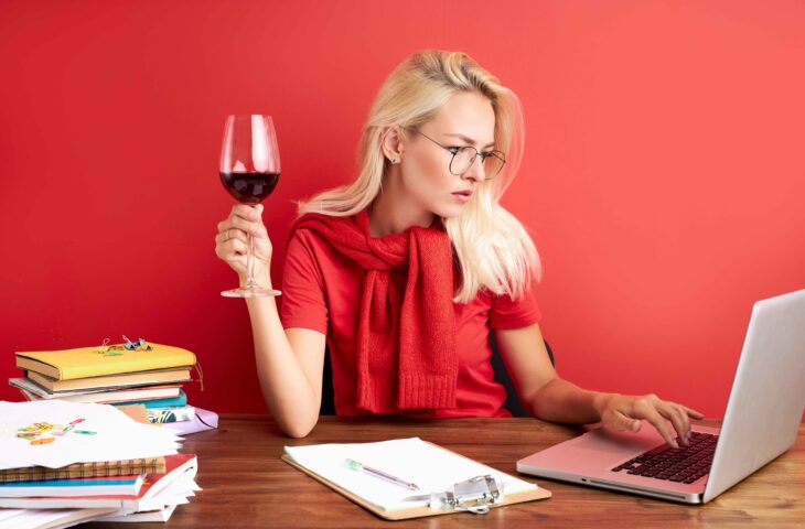 Une femme travaille sur son ordinateur avec un verre de vin rouge à la main