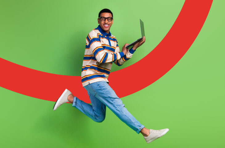 Un jeune homme joyeux saute avec un ordinateur portable à la main sur un fond coloré vert