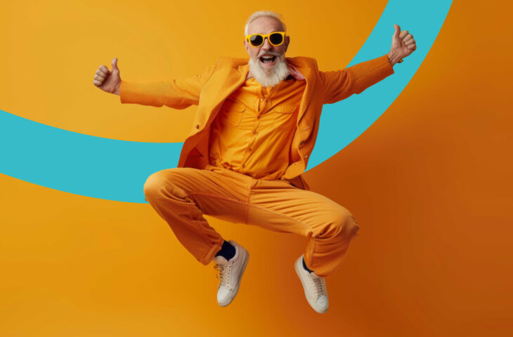 Un homme senior, en costume jaune et lunettes de soleil, saute de joie sur un fond coloré