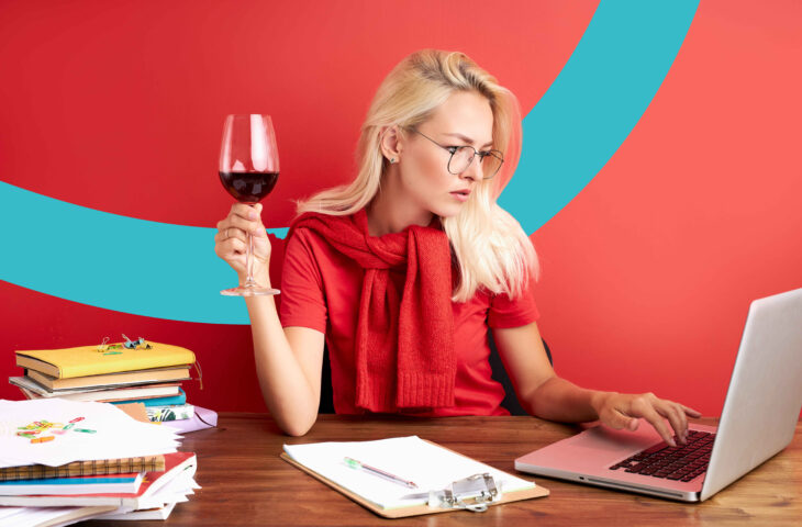 Une femme travaille sur son ordinateur avec un verre de vin rouge à la main